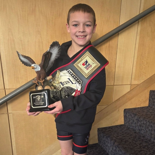 Smiling young wrestler holding an Outstanding Wrestler eagle trophy and a USA Wrestling championship belt