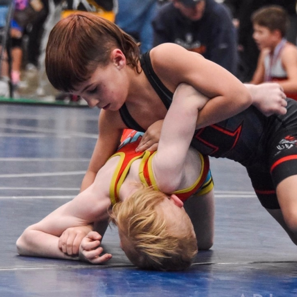Young wrestler working to turn an opponent on the mat at a youth tournament
