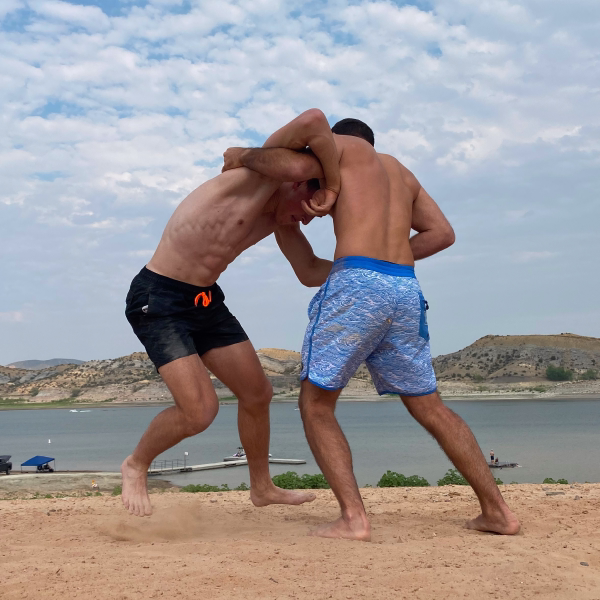 Two wrestlers locked up in a beach wrestling match on the sand beside a lake